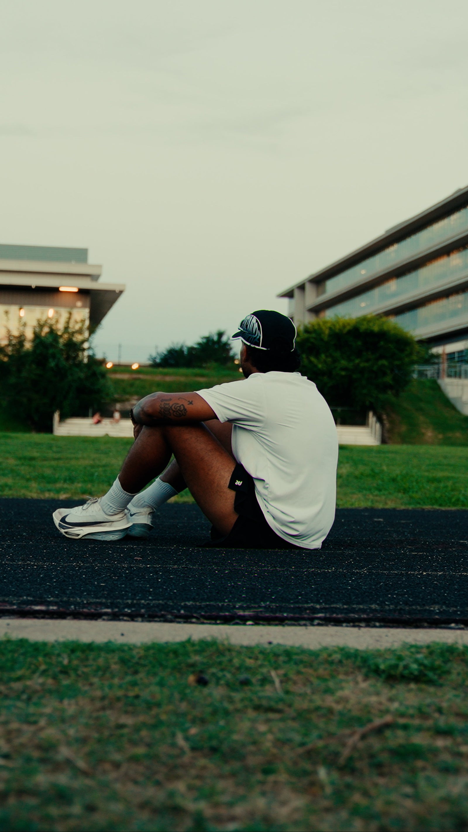 Person sitting on a track in an outdoor setting with buildings in the background