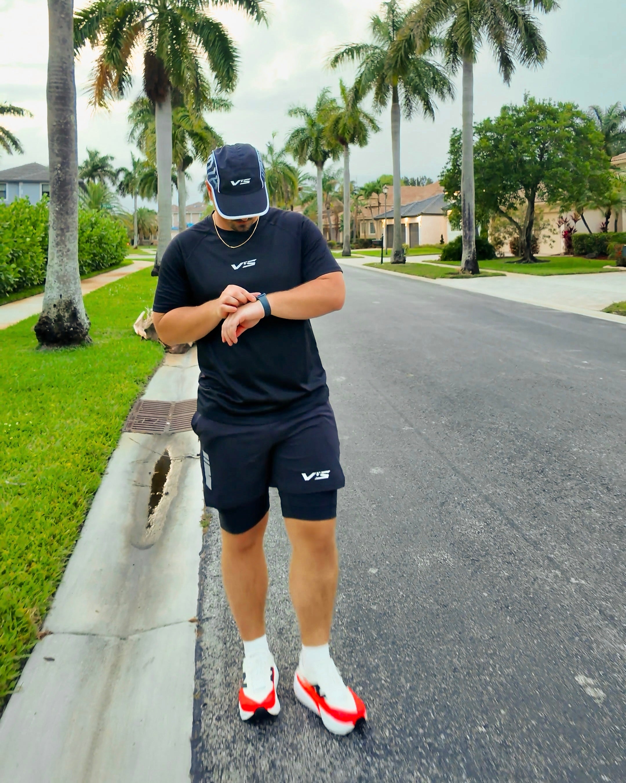 Person in athletic wear checking their watch on a suburban street with palm trees.