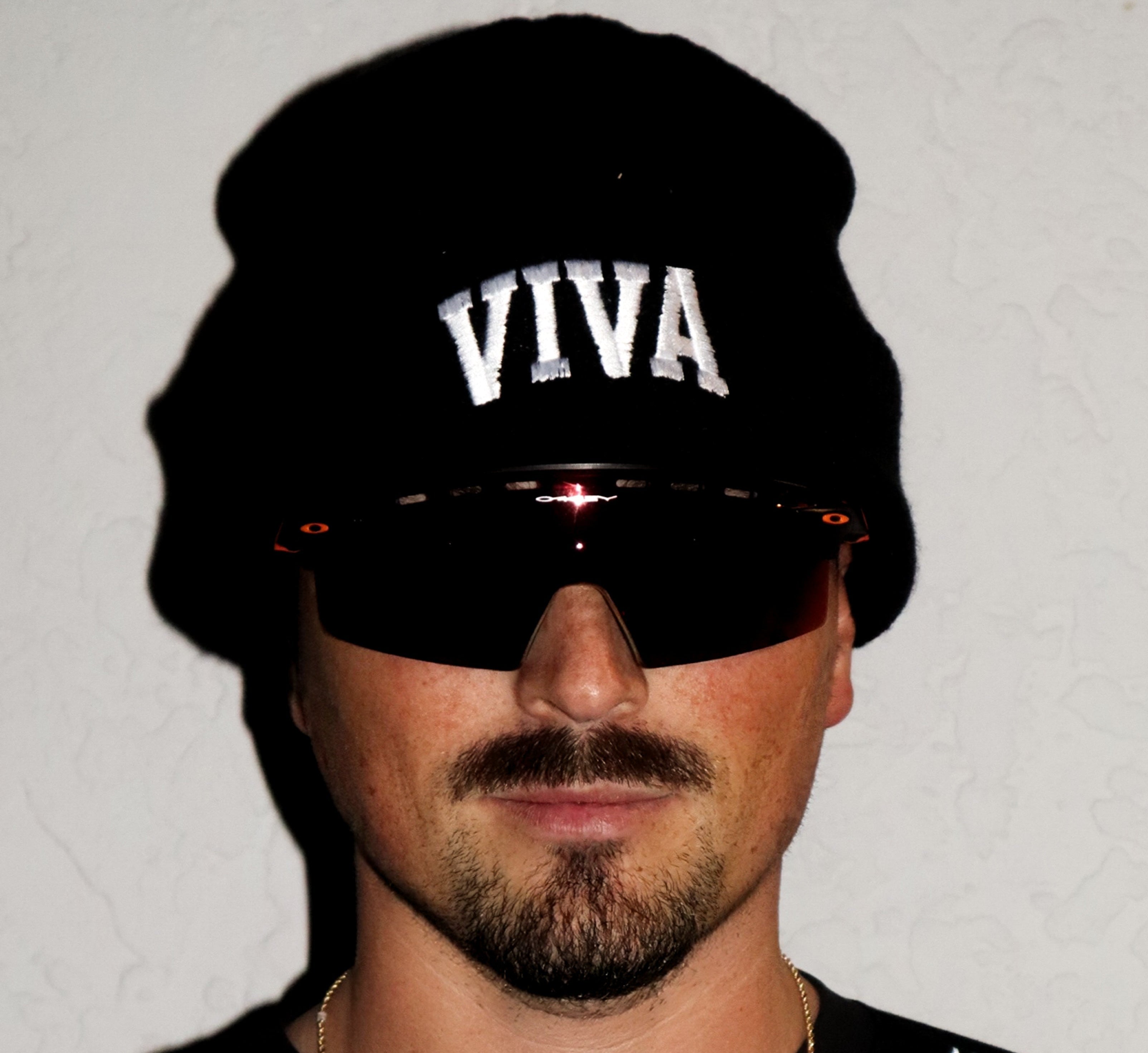 Person wearing a black beanie with 'VIVA' text and sunglasses on a plain background